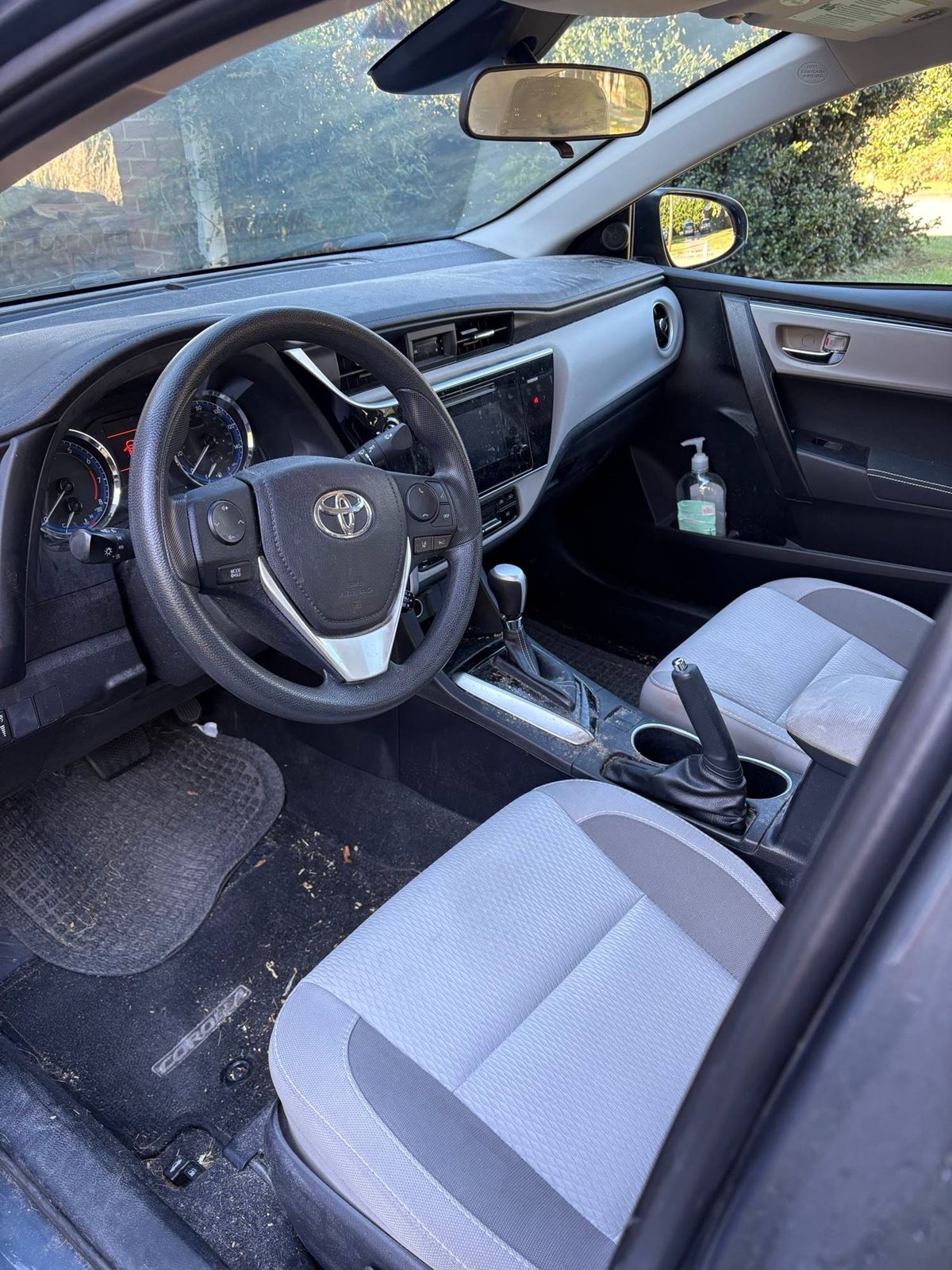 Toyota Corolla interior before detailing: dusty dash and debris across the console and floor